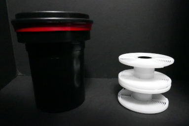 A black developing tank with a red lid next to two white film reels stacked vertically.